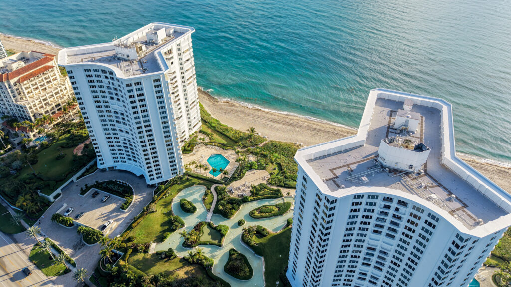 Angled drone photo of the Chalfonte oceanfront condo towers in Boca Raton, Florida, showing the beach, lagoon style grounds, and Atlantic Ocean.
